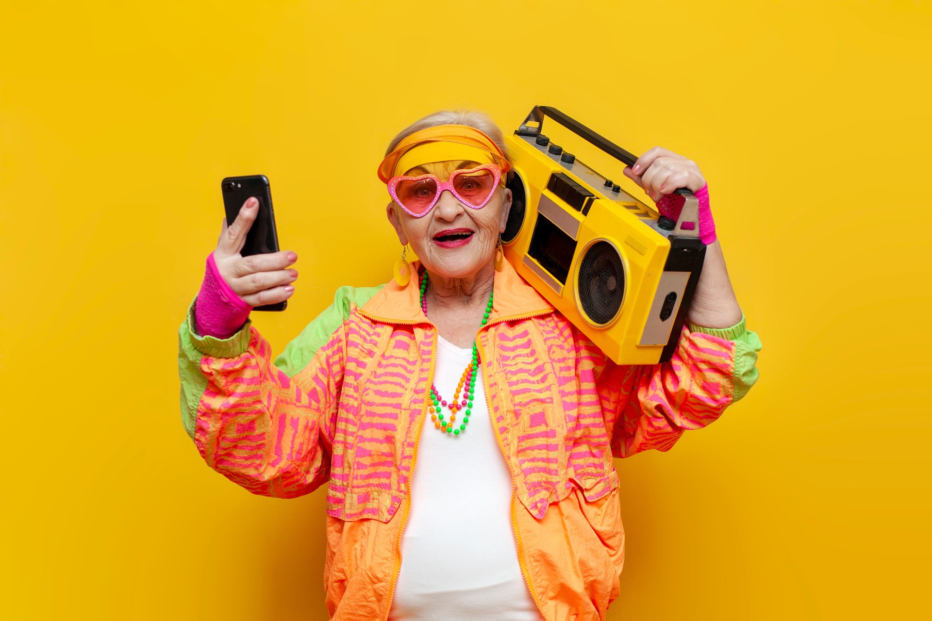 crazy old grandmother with tape recorder and smartphone in hipster clothes listens music on yellow background